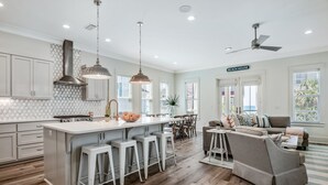 A modern kitchen with a large island, bar stools, and pendant lighting.
