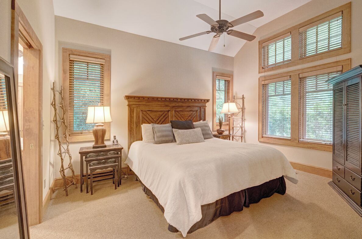 A bedroom with a large bed, wooden headboard, two bedside tables with lamps, and a ceiling fan.