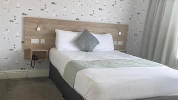 Ein ordentlich gemachtes Bett mit einem Holz-Kopfteil, einem grauen Kopfkissen und einer weißen Decke.