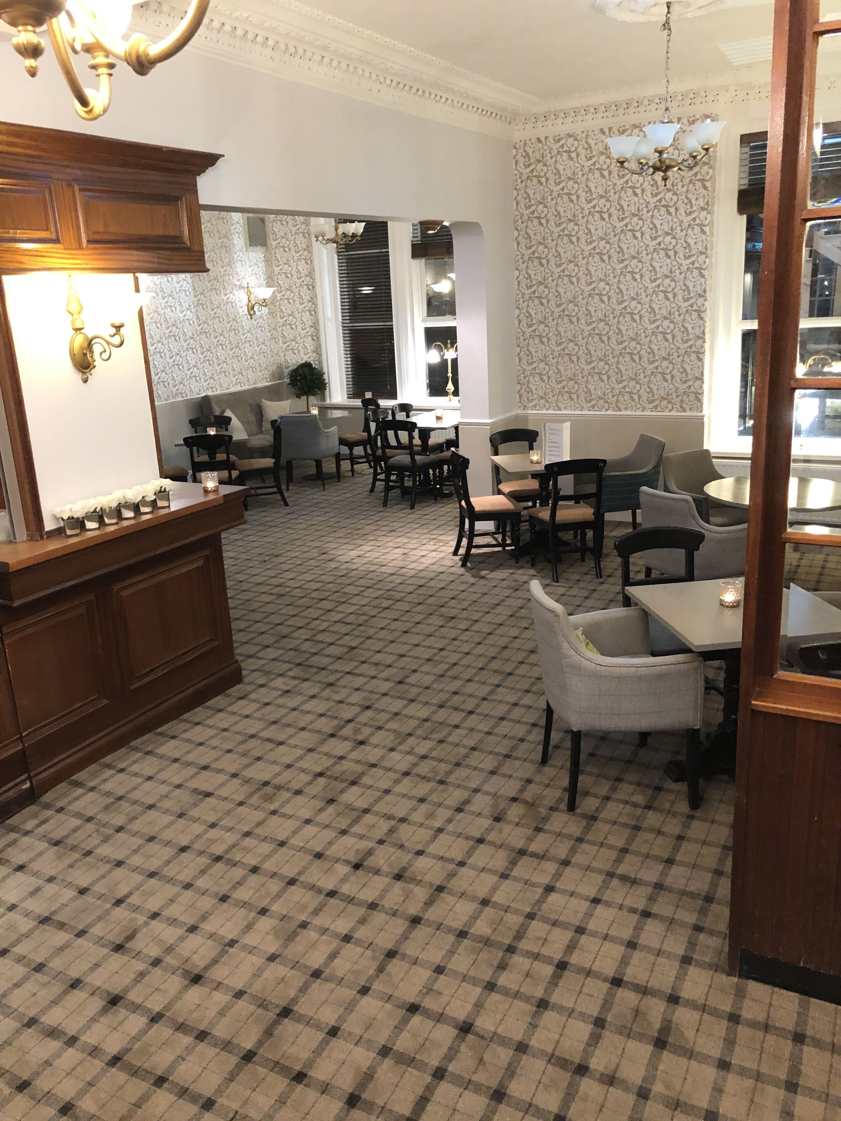 A dining area with checkered flooring, wooden furniture, and patterned wallpaper.