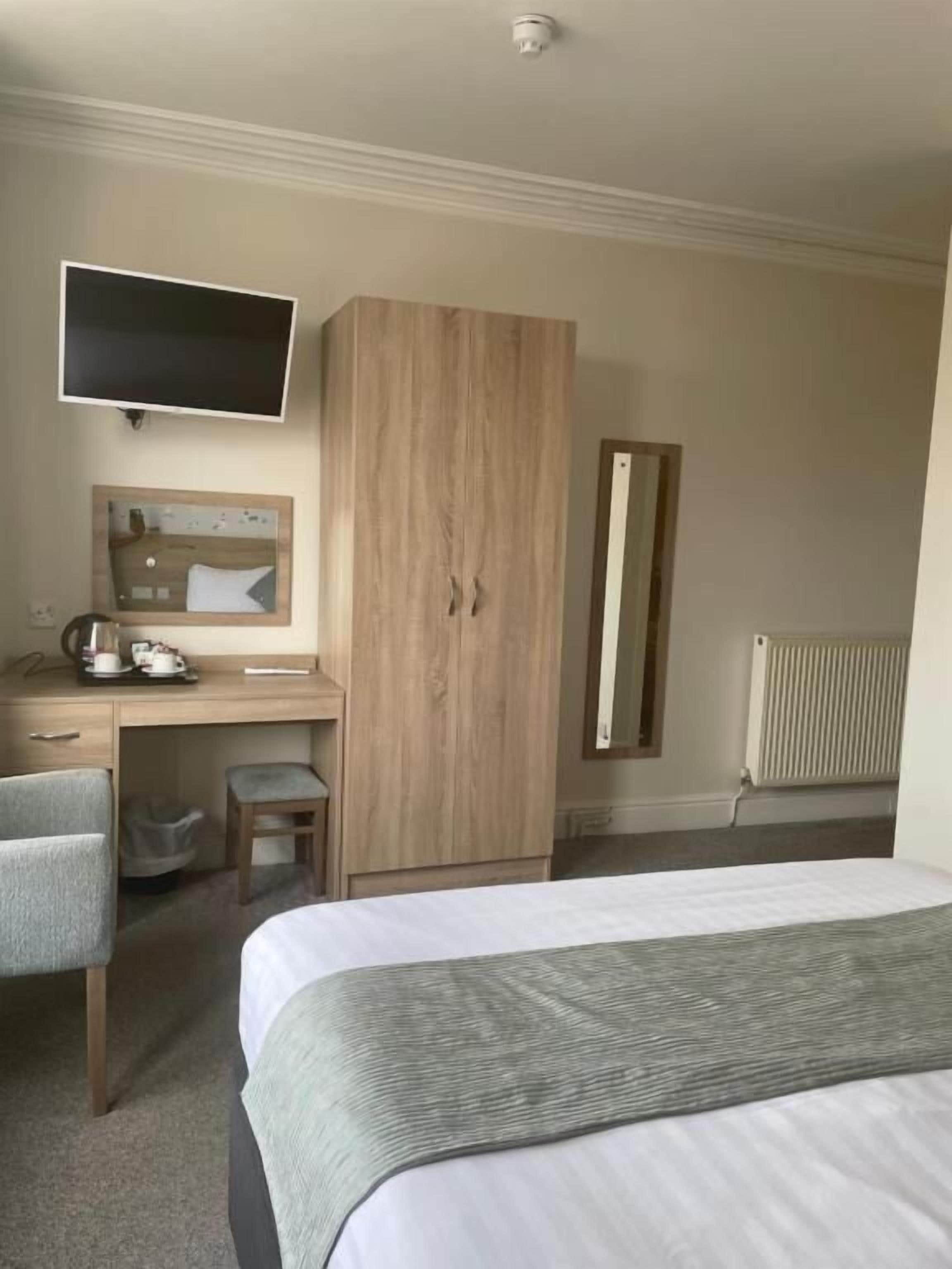 A hotel room with a bed, a desk, a chair, a television, a wardrobe, and a radiator.