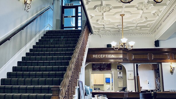 A grand staircase leading to a reception area with ornate ceiling details and a chandelier. - The Clarendon Hotel (Morecambe)