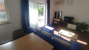 A modern living room with a sofa set, a dining table, a TV, and a plant. - Anica Apartmani (Funtana)