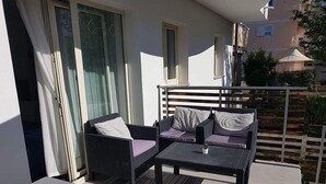 A balcony with a sofa and a small table, a window, and a view of a building. - Anica Apartmani (Funtana)