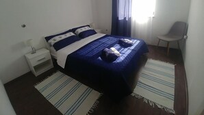 A bedroom with a bed, a chair, a nightstand, and a window with curtains. - Anica Apartmani (Funtana)