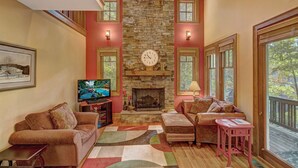 A cozy living room with a stone fireplace, comfortable seating, and large windows offering a view of the outdoors. - A Foxfire Retreat: Gated Resort w/ Pools & Hot Tub, Fishing, Fitness Area (Boone)
