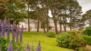 Un jardin bien entretenu, avec une variété de plantes et d’arbres, une pelouse soigneusement taillée et, au fond, un bâtiment au style architectural traditionnel.