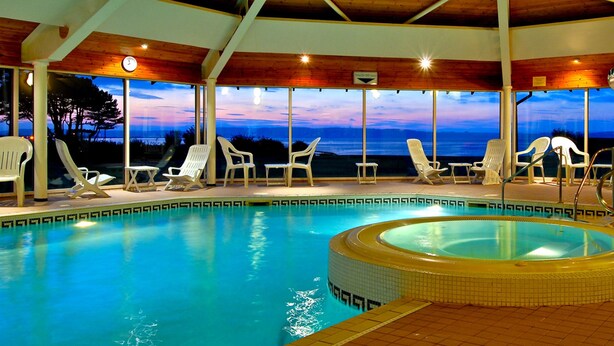 Un espace piscine doté d’un jacuzzi, de chaises longues et offrant une vue sur l’océan au crépuscule.