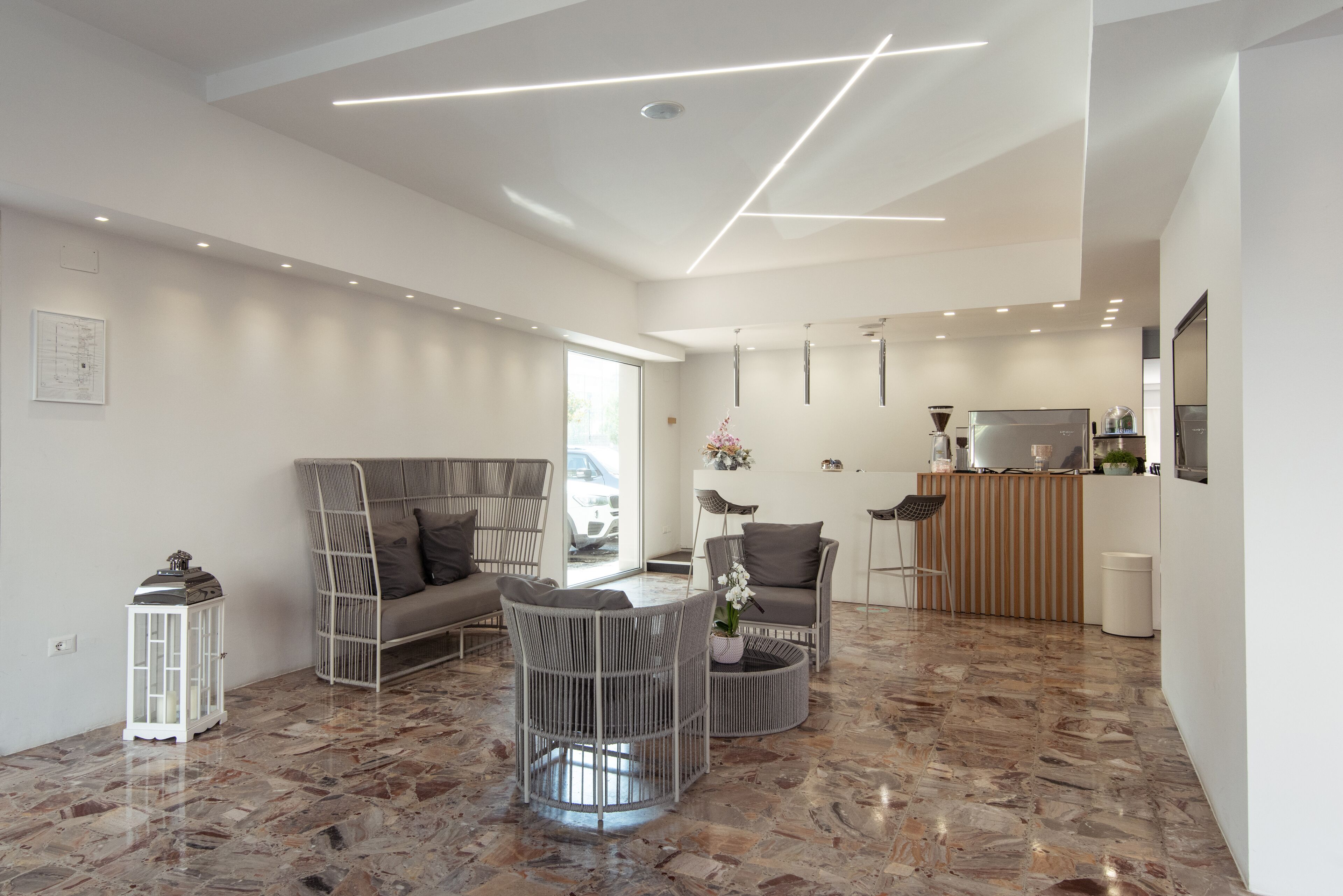 Una sala de estar moderna con sofá, sillas, una mesa de centro y una zona de cocina con mostrador y electrodomésticos.