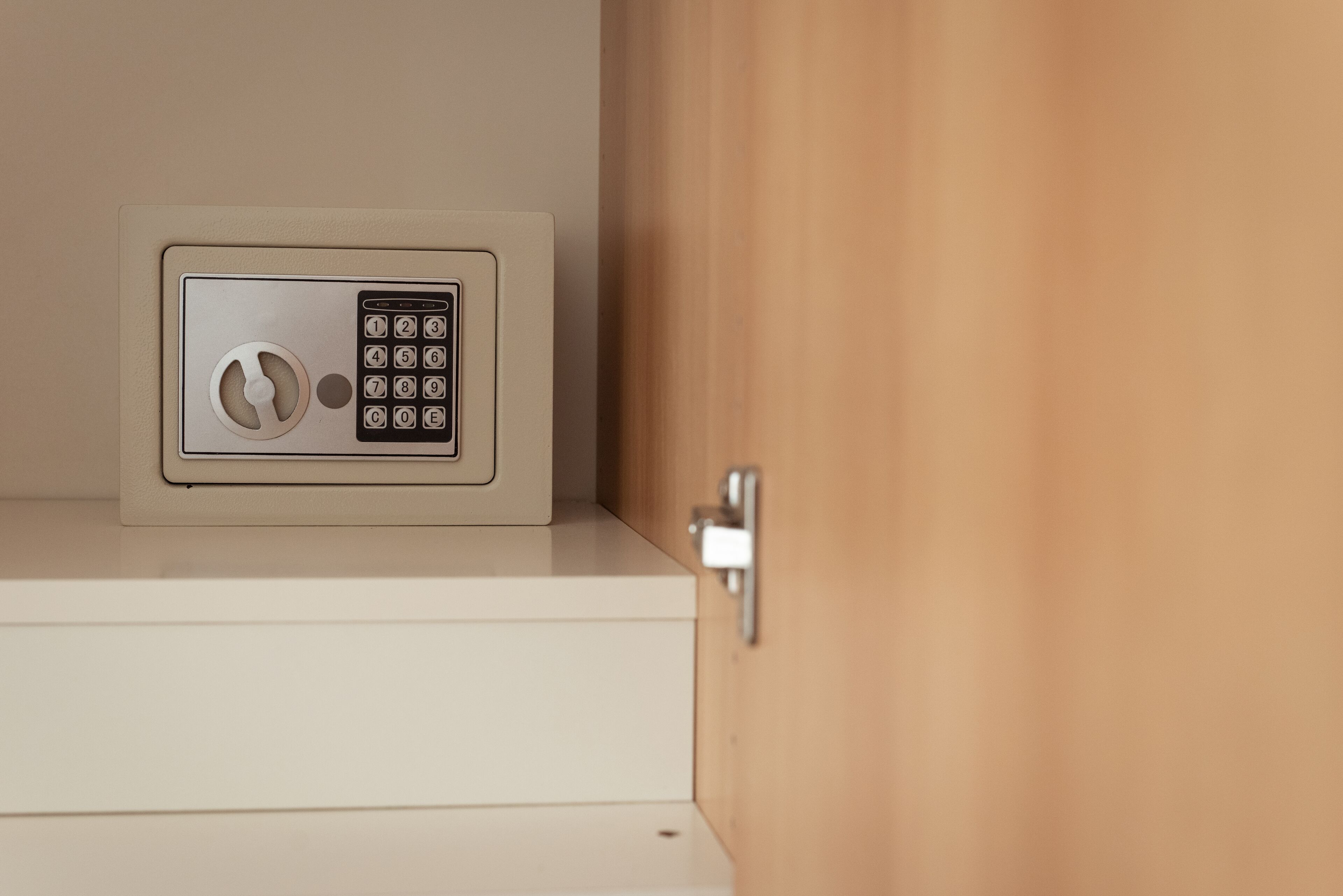 A safe with a keypad on a white cabinet, a door handle, and a wooden door.