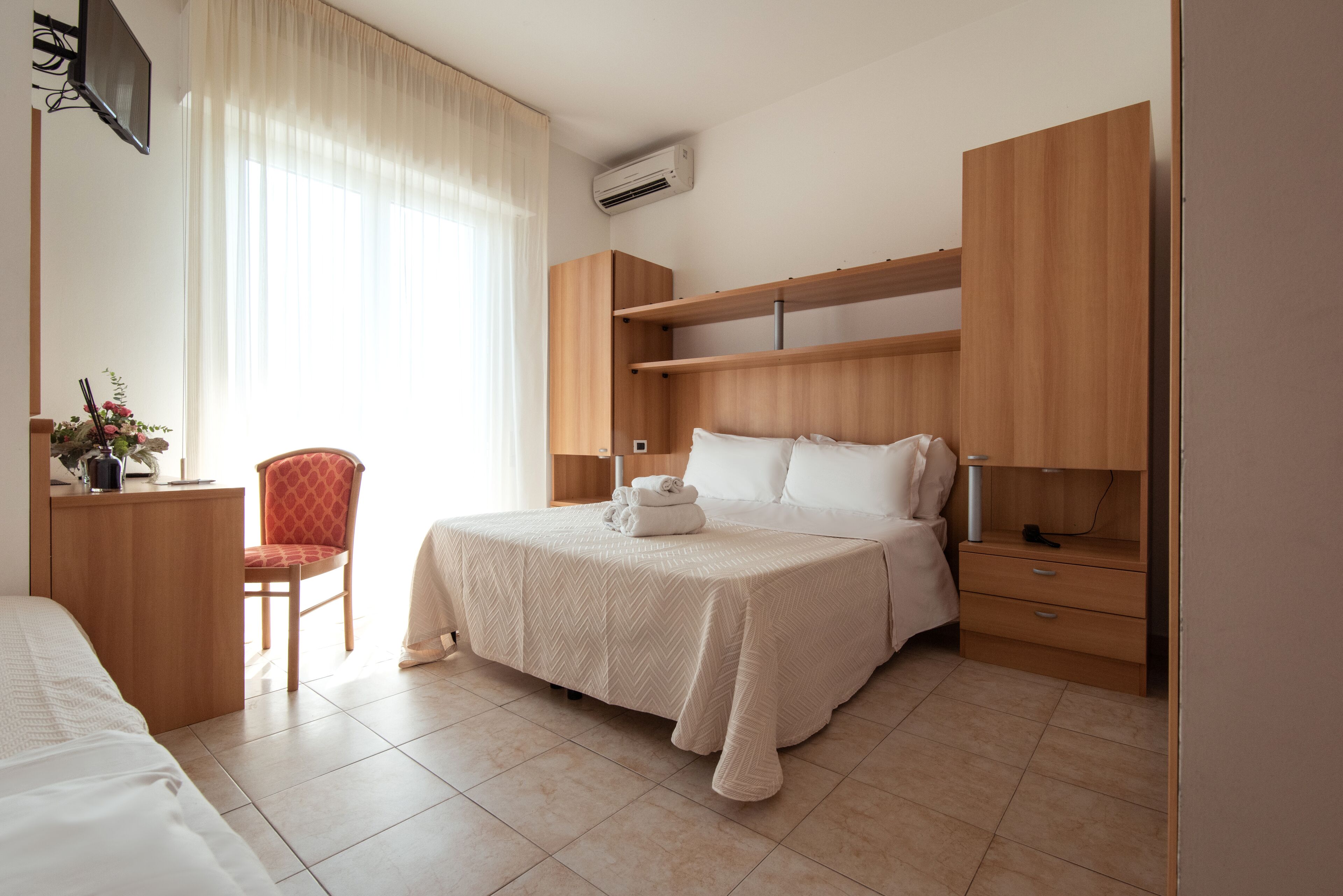 A neatly arranged bedroom with a bed, bedside tables, a chair, and a desk.