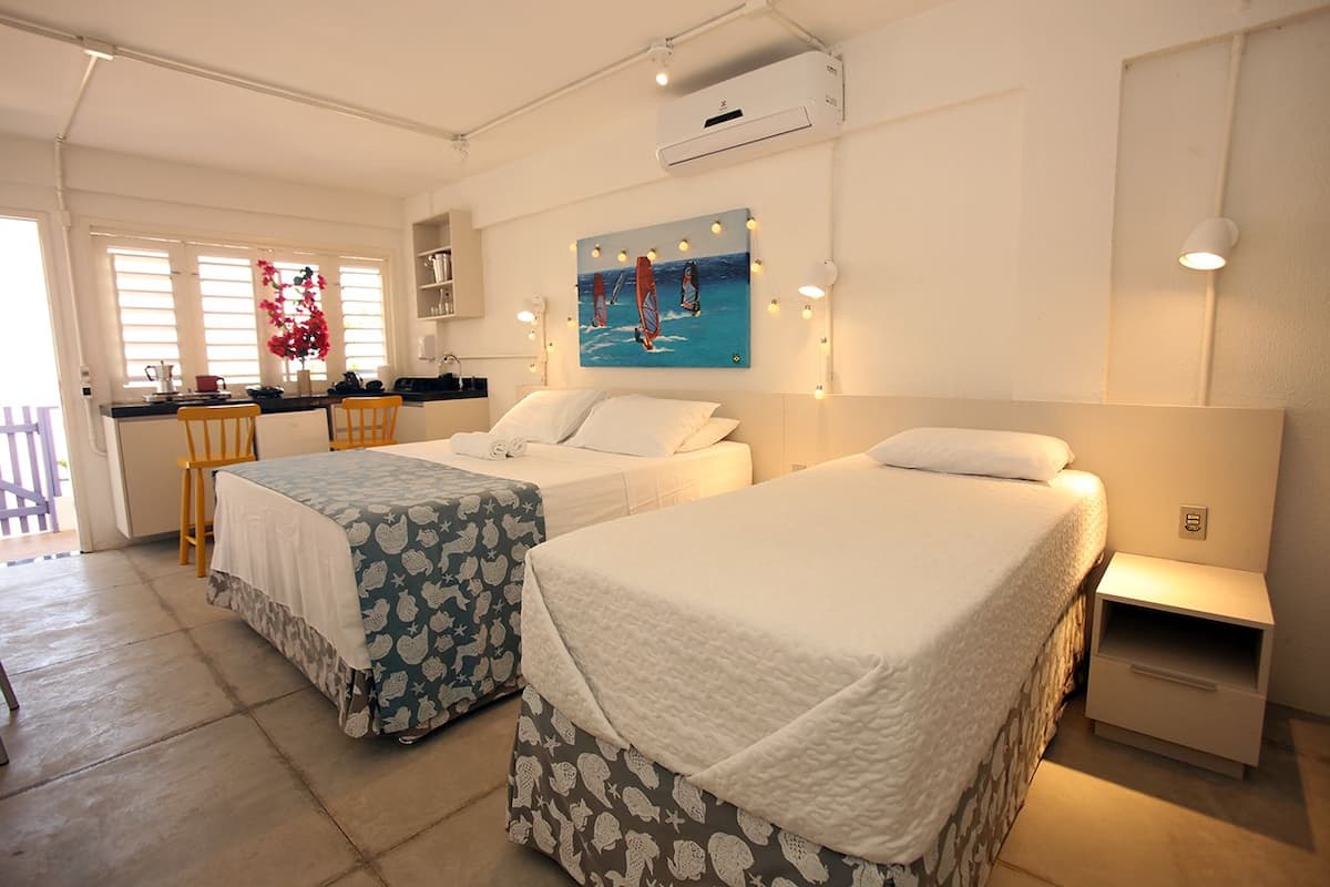 A hotel room with two beds, a kitchenette, and a painting of windsurfers.