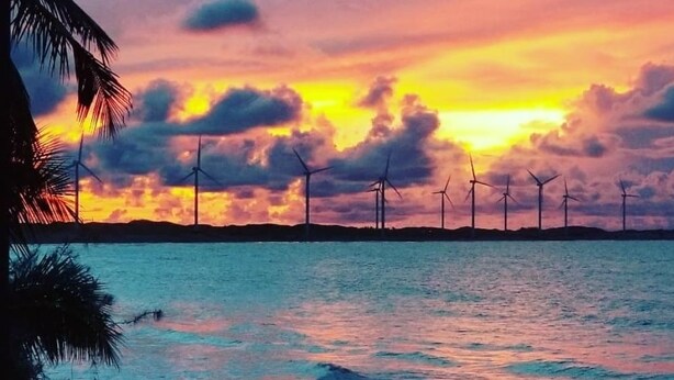 A sunset over a coastal area with wind turbines in the distance. - Saint Germain Kite Residence (Amontada)