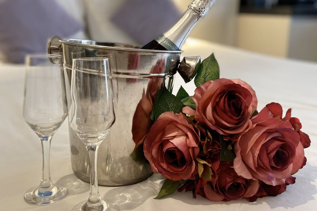 A table with a champagne bottle, two wine glasses, and a bouquet of roses.