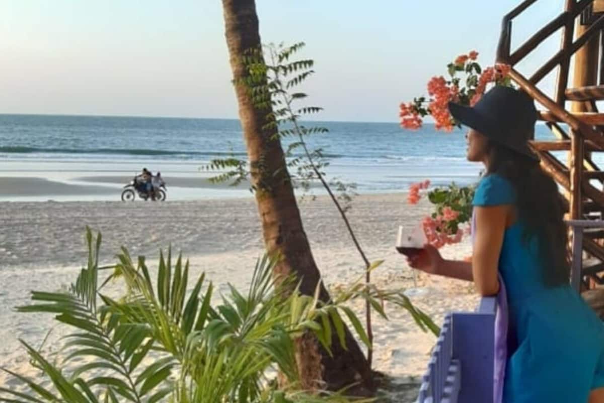 A beach view with a person holding a phone, palm trees, and a railing.
