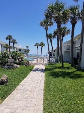 Stroll along the pathway to the resort's inviting pool area, surrounded by lush greenery and palm trees.