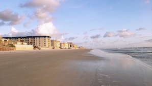 En strand med en rad höga byggnader, inklusive ett hotell med balkonger och en gångväg som leder ner till stranden.