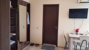 Une chambre d’hôtel équipée d’une armoire, d’une porte, d’un téléviseur fixé au mur, d’un bureau avec une chaise et d’une paire de chaussons posés sur le sol.