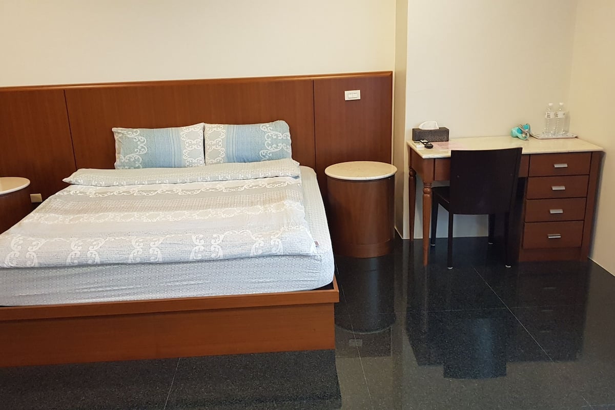 A bedroom with a wooden bed, two bedside tables, a desk with a chair, and a small cabinet.