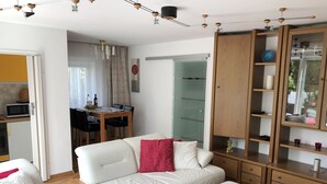 A modern living room with a white sofa set, a wooden cabinet with glass doors, and a dining area with a table and chairs. - Ferienwohnung Dettum (Dettum)