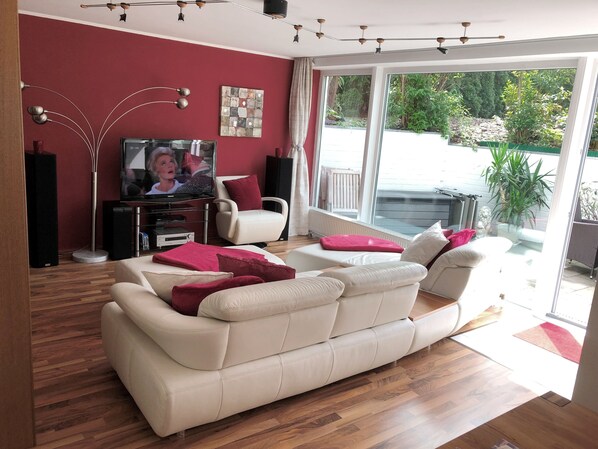 A living room with a beige sofa, a television, and a large window. - Ferienwohnung Dettum (Dettum)