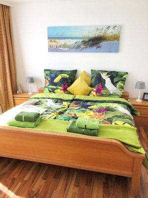A neatly made bed with green and yellow floral bedding, a tropical-themed pillow, and a small decorative item on the nightstand. - Ferienwohnung Dettum (Dettum)