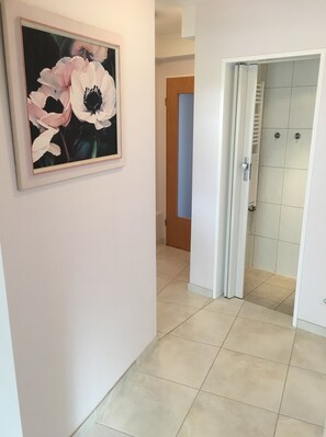 A hallway with a framed floral painting on the wall, a door leading to a bathroom, and a tiled floor. - Ferienwohnung Dettum (Dettum)
