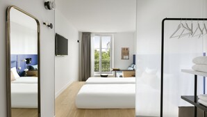 Ein Hotelzimmer mit zwei Betten, einem Fernseher, einem Fenster mit Aussicht, einem Spiegel und einem Kleiderhaken.