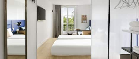 A hotel room with two beds, a TV, a window with a view, a mirror, and a hanging clothes rack.