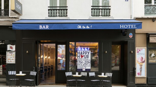 Eine Bar und ein Hotel mit blauem Markisenvorzelt, Außenbestuhlung und einem Schild mit der Aufschrift 'Happy Hour'.