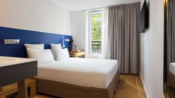 Habitación de hotel con una cama grande, un escritorio, un televisor de pantalla plana y un ventanal con cortinas.