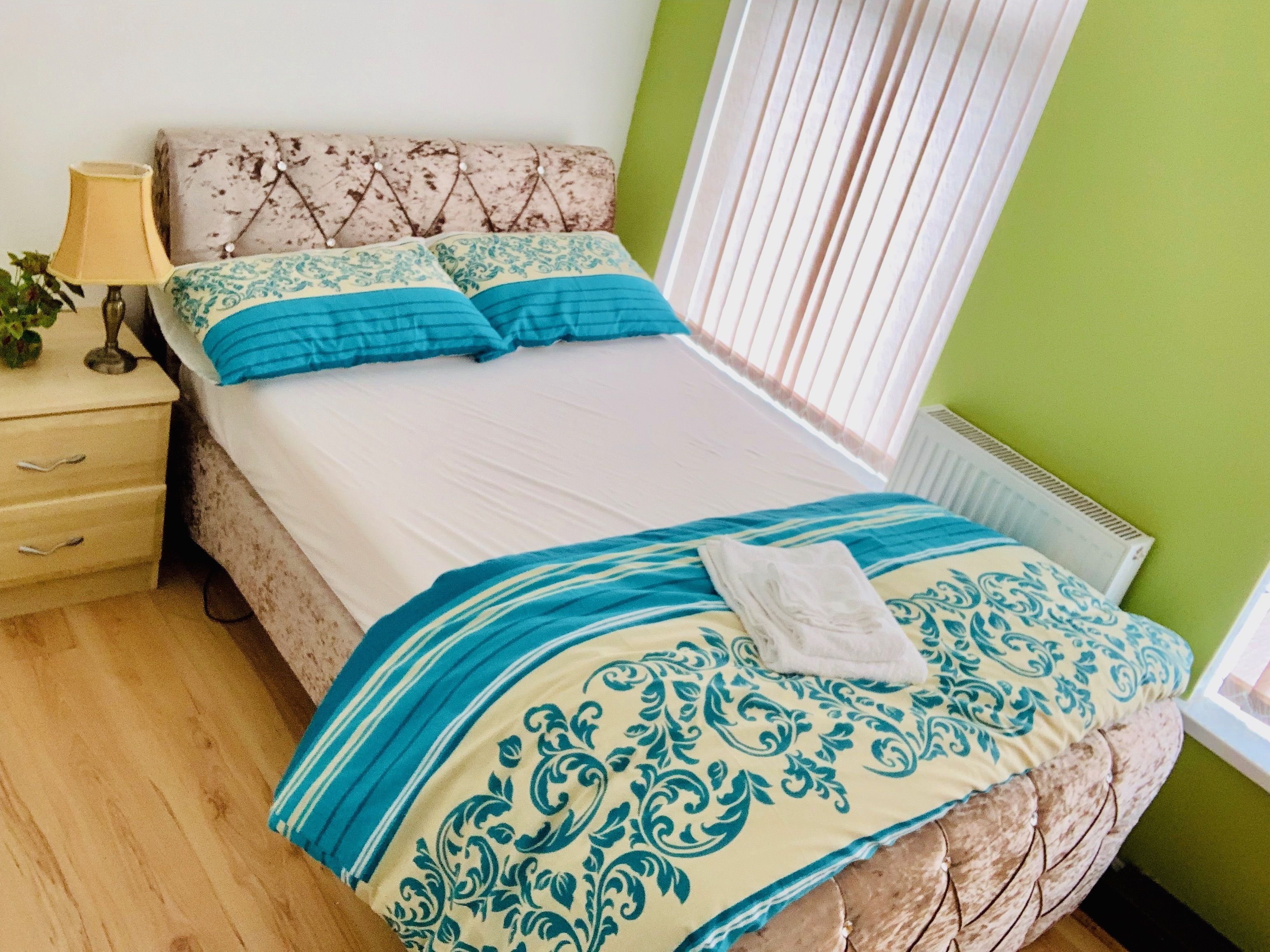 A neatly made bed with a patterned bedspread and pillows, a bedside lamp, and a nightstand with drawers.