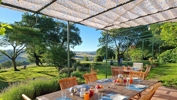An outdoor dining area with a table set for two, surrounded by chairs, under a patterned canopy. - La Basserie (Laguepie)