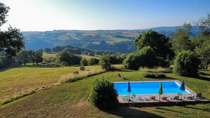 A pool area with lounge chairs and a view of rolling hills. - La Basserie (Laguepie)