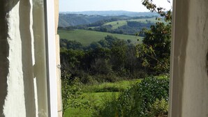 A room with a large window offering a view of rolling hills and greenery. - La Basserie (Laguepie)
