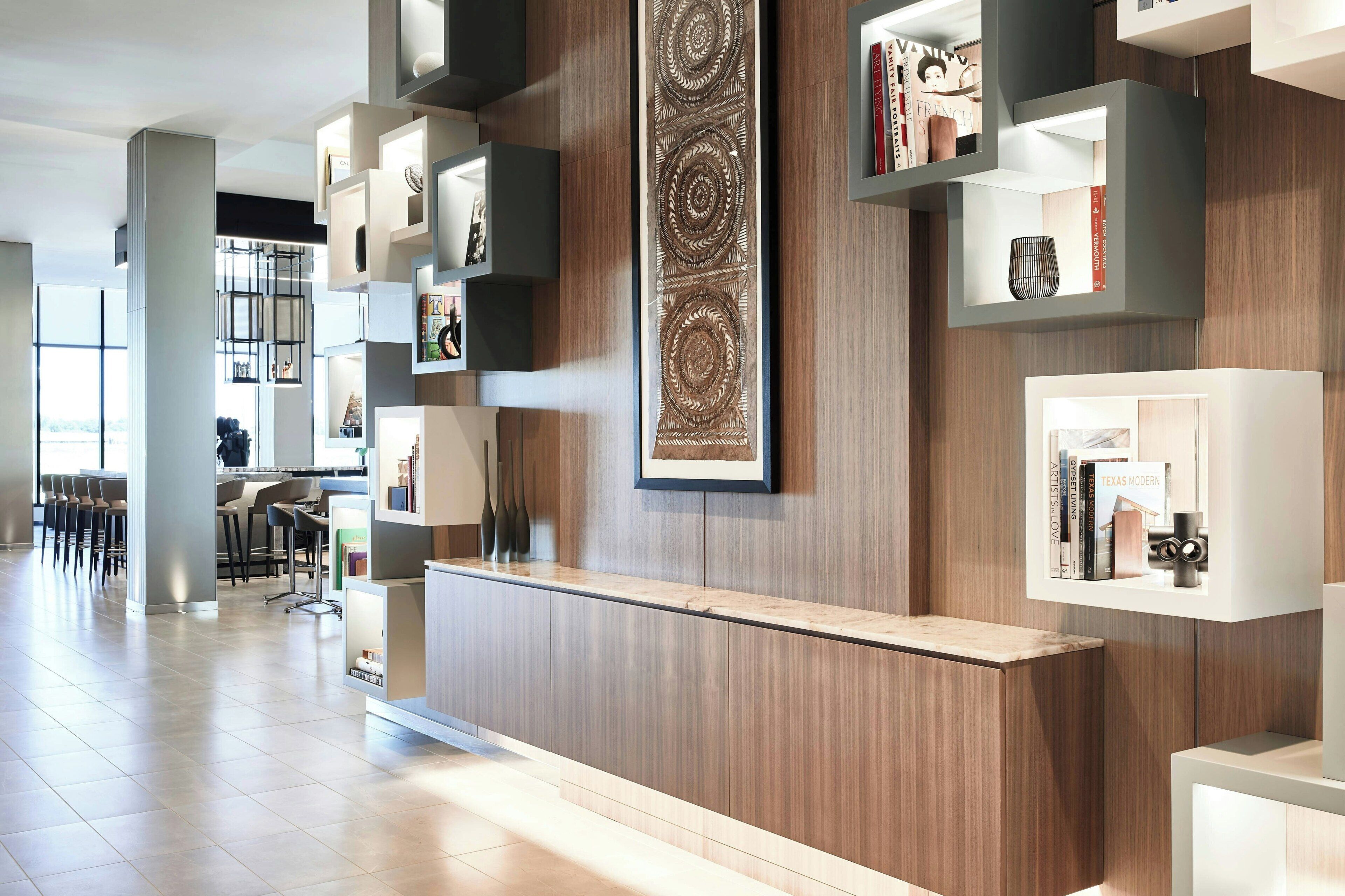 A modern reception area with a wooden reception desk, built-in shelving with books and decorative items, and a large wall-mounted artwork.