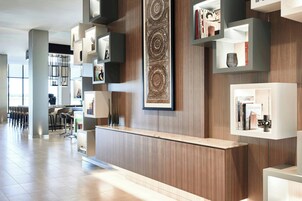 Un área de recepción moderna con un mostrador de madera, estanterías integradas con libros y objetos decorativos, y una obra de arte grande colgada en la pared.