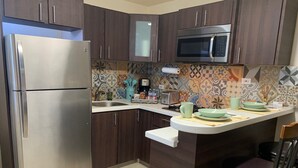 A kitchen with dark wooden cabinets, a stainless steel refrigerator, a microwave, and a small island with a chair. - Charming Retreat with Patio Access and Laundry (Ponce)
