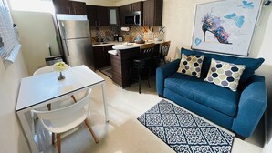 A compact living space with a kitchenette, a dining area, and a sofa with patterned cushions. - Charming Retreat with Patio Access and Laundry (Ponce)