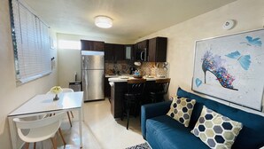 A compact kitchen with a refrigerator, microwave, and a small dining area with a table and chairs. - Charming Retreat with Patio Access and Laundry (Ponce)