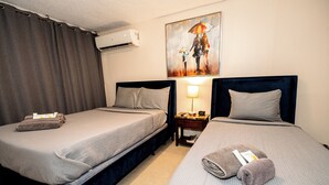 A hotel room with two beds, a painting on the wall, an air conditioner, and a nightstand with a lamp. - Charming Retreat with Patio Access and Laundry (Ponce)