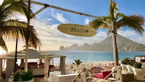 A beach club with a sign reading "CACHET BEACH CLUB" and a view of the sea and mountains in the background. - PARTY on Cabo Villas & Mango Deck Executive Suite (El Medano)