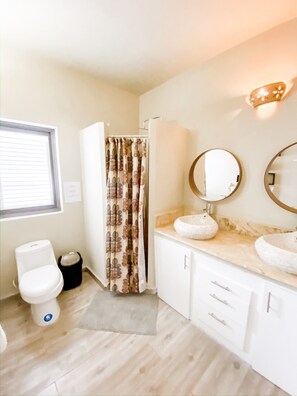A bathroom with a toilet, a sink with a round mirror, a shower curtain, and a light fixture on the wall.
