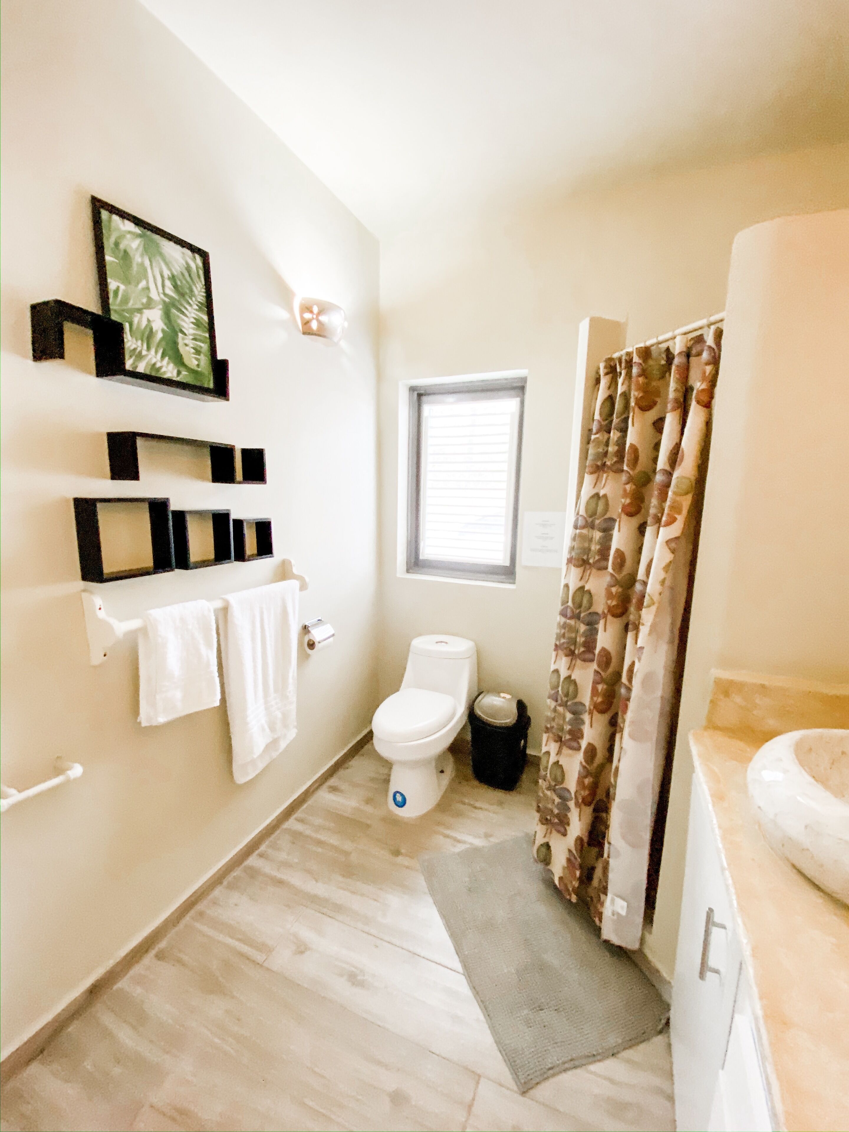 A bathroom with a toilet, a window, a shower curtain, and a towel rack with towels.