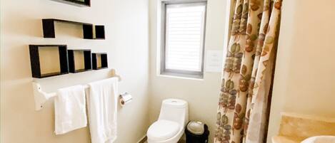 A bathroom with a toilet, a window, a shower curtain, and a towel rack with towels.