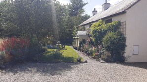 A gravel driveway leading to a house with a sloped roof and a small garden area with potted plants and a bench. - 300 Year old Tradition Irish Cottage (Rathkeale)