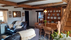 A cozy living room with a dark leather sofa, a wooden dining table, and a staircase with wooden railings. - 300 Year old Tradition Irish Cottage (Rathkeale)