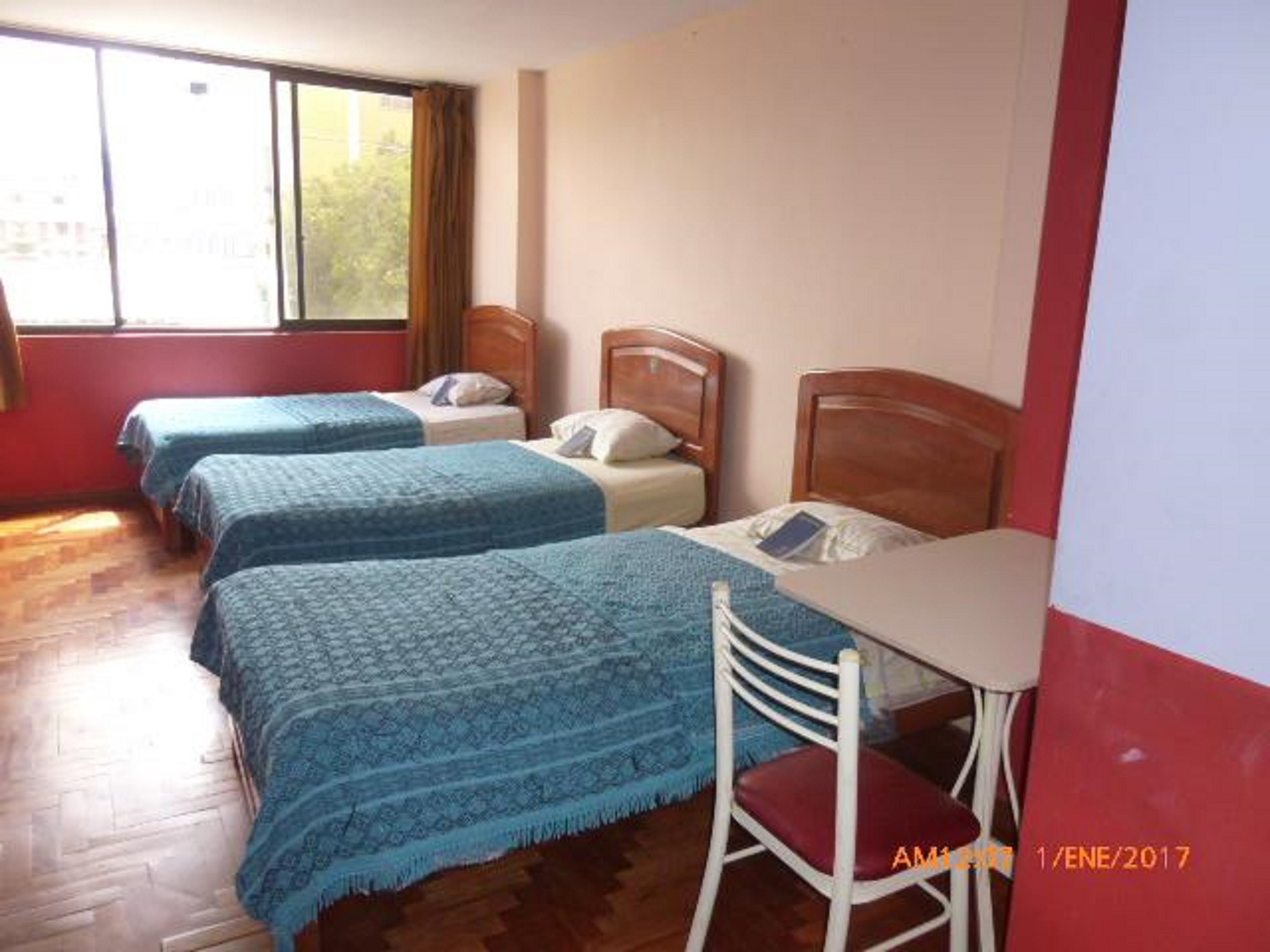 A room with three beds, a wooden desk, and a chair.