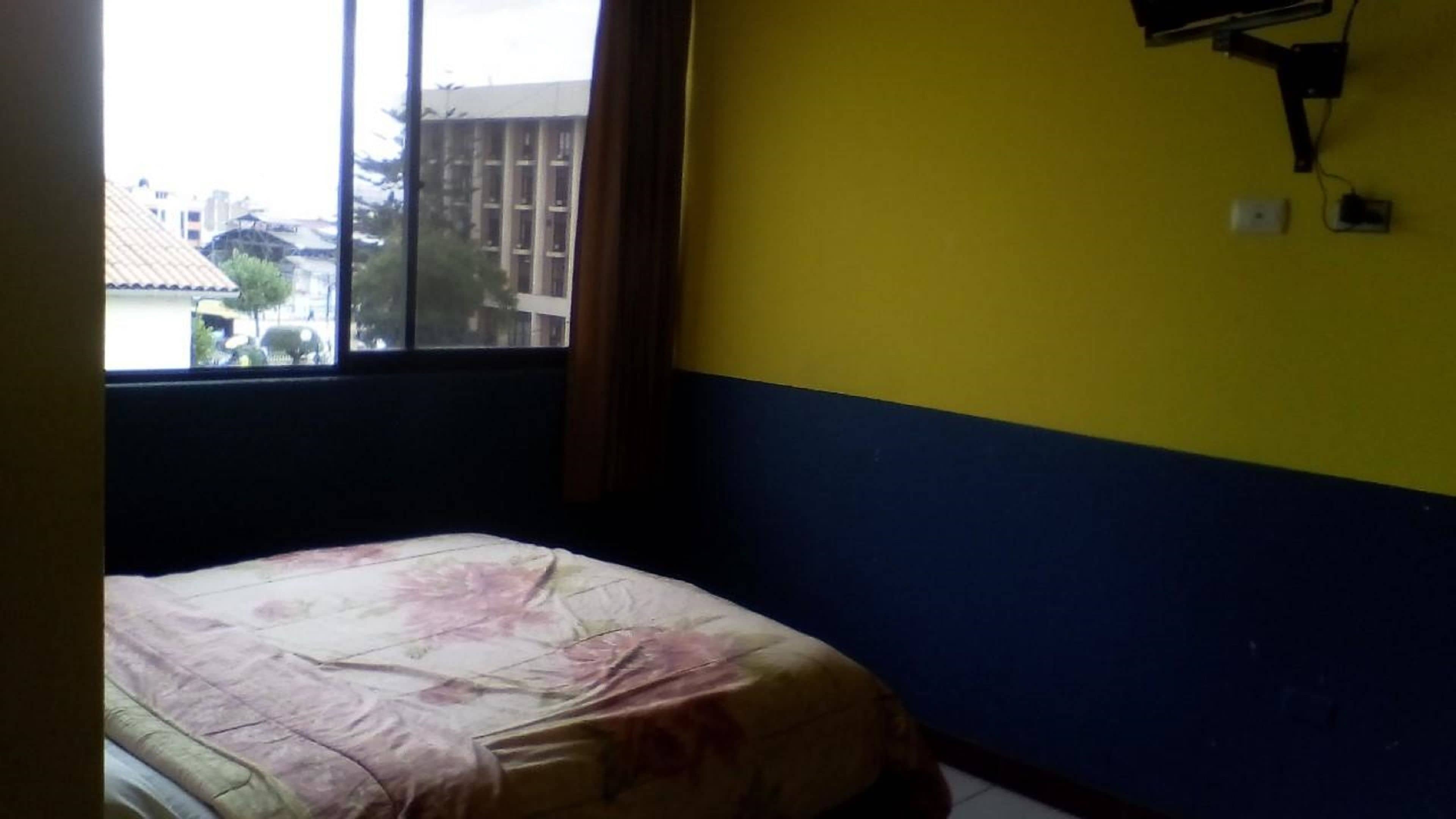 Una habitación pequeña con una cama, un ventanal y aire acondicionado instalado en la pared.