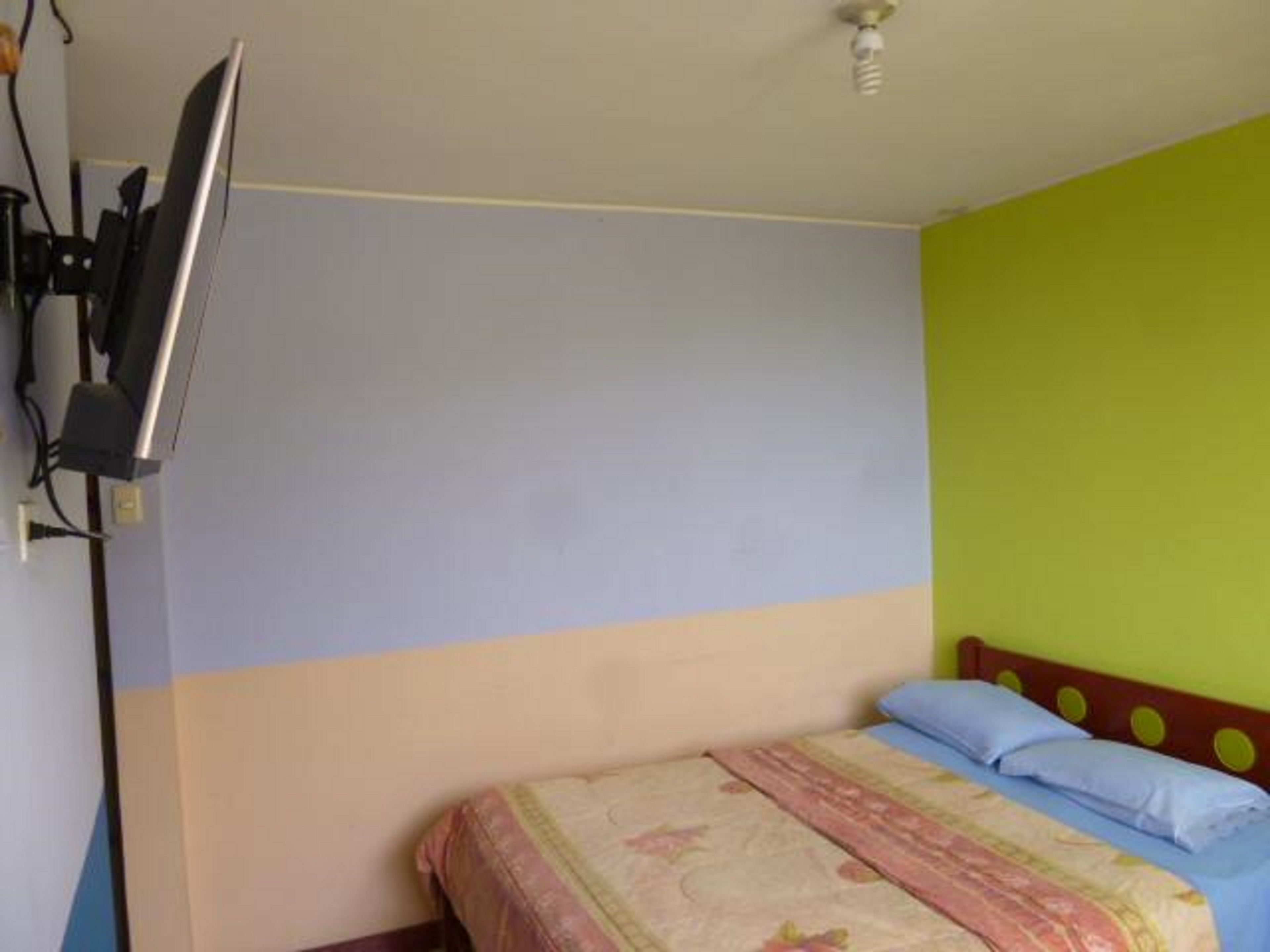 A bedroom with a bed, a television mounted on the wall, and a ceiling light.